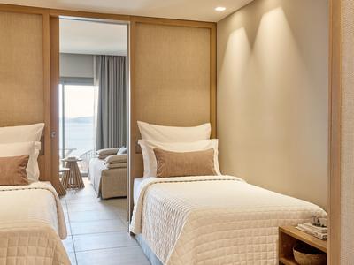 Modernes Schlafzimmer mit zwei Einzelbetten, beiger Wand, Spiegel und hellen Vorhängen.