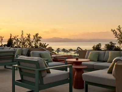 Área de descanso al aire libre con sofás y sillas al atardecer junto al mar