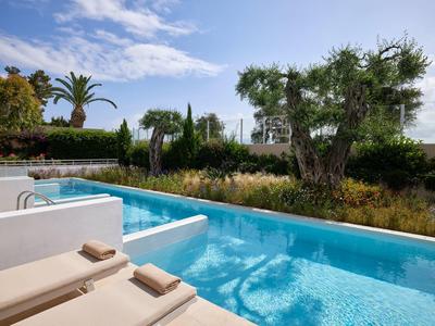 Moderner Außenpool mit blauer Wasserfläche, Sonnenliegen und grüner Bepflanzung im Hintergrund.