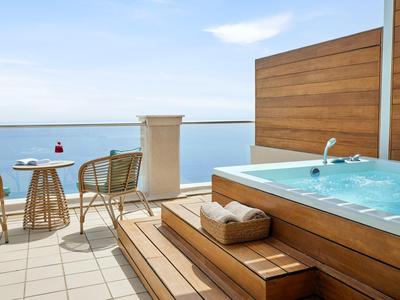 Luxuriöse Terrasse mit Holz-Whirlpool, zwei Stühlen, kleinem Tisch und Meerblick bei Tageslicht.