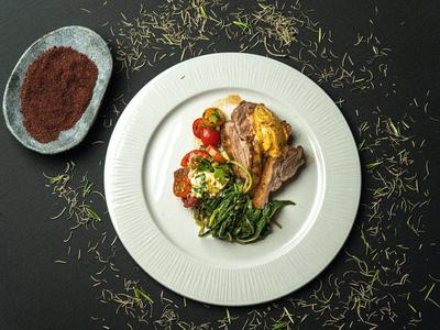 Teller mit gebratenem Fleisch, grünem Gemüse, Kartoffeln und Tomaten, daneben Schale mit Gewürz.