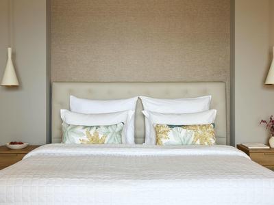 Schlichtes Schlafzimmer mit weißem Bett, zwei Blumenmustern auf Kissen und minimalistischem Holztisch.