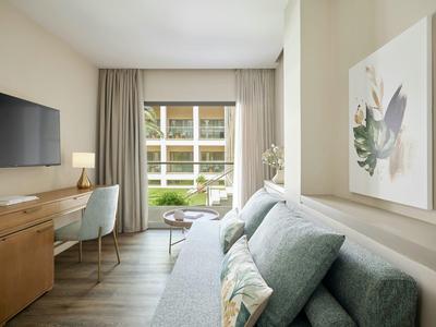 Helles Wohnzimmer mit Sofa, großem Fenster, Schreibtisch, Fernseher und natürlicher Dekoration.