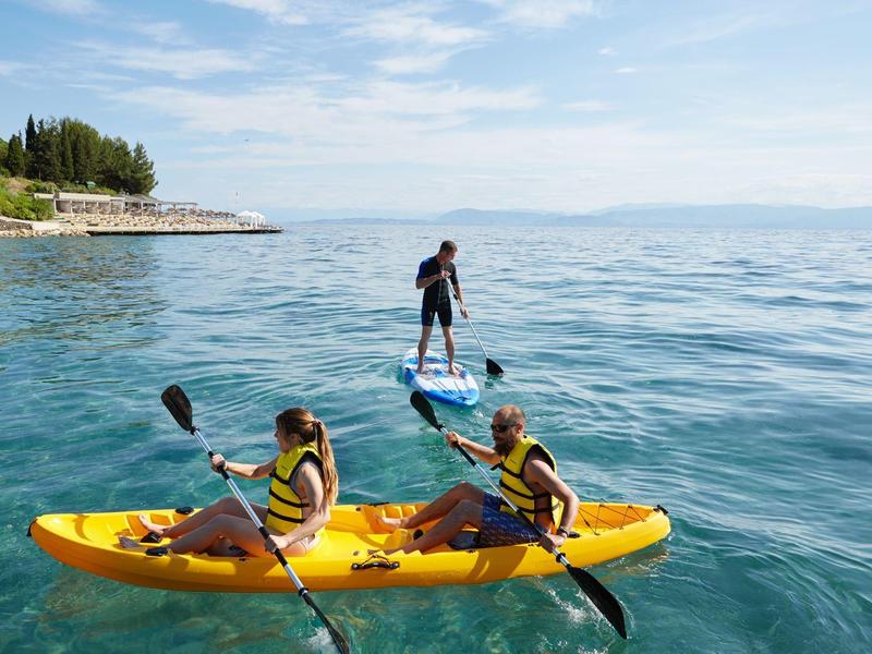 Menschen paddeln im gelben Kajak und stehen auf einem Paddleboard im klaren blauen Meer.