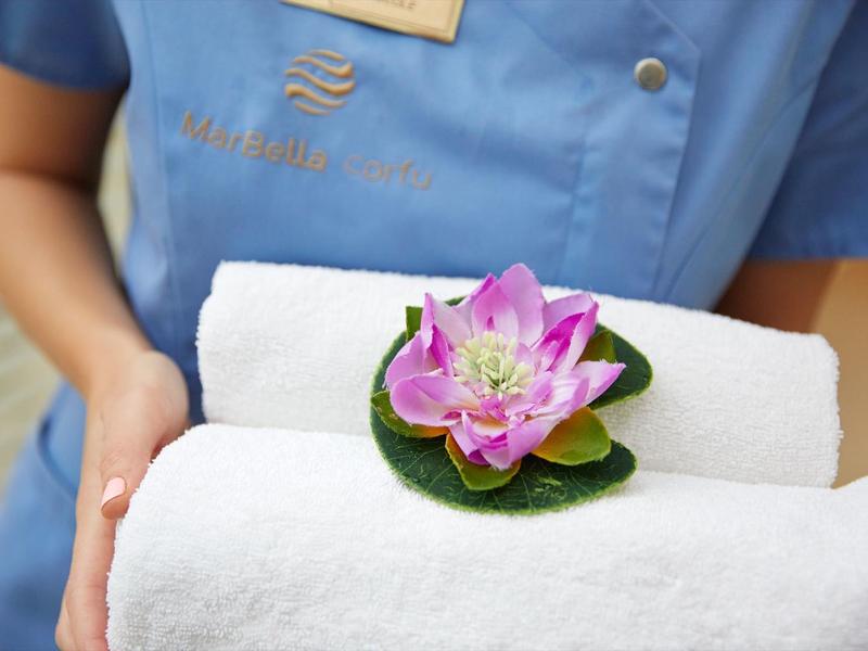 Person hält weiße, gefaltete Handtücher mit einer lilafarbenen Lotusblume darauf.