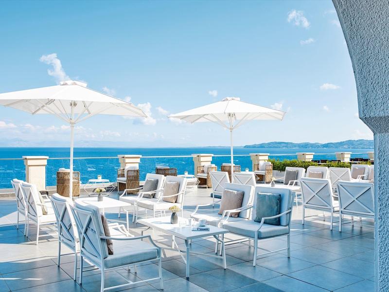 Terrassenbereich mit weißen Möbeln und Sonnenschirmen, Blick auf blauen Himmel und Meer.