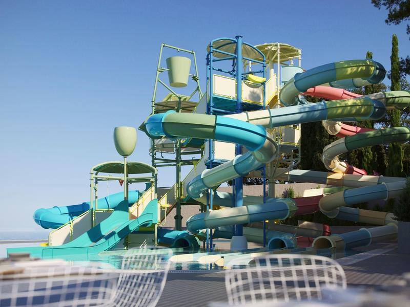 Wasserpark mit bunten Rutschen und transparenten Sitzstühlen bei klarem Himmel.