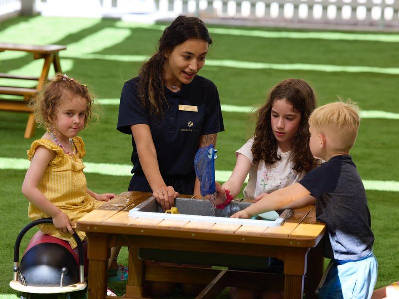 Eine Frau und drei Kinder sitzen an einem Holztisch im Freien und beschäftigen sich gemeinsam.