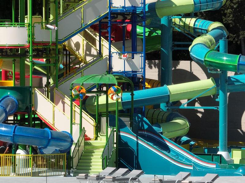 Wasserpark mit bunten Wasserrutschen, Treppen und Geländern in Blau, Grün und Gelb.