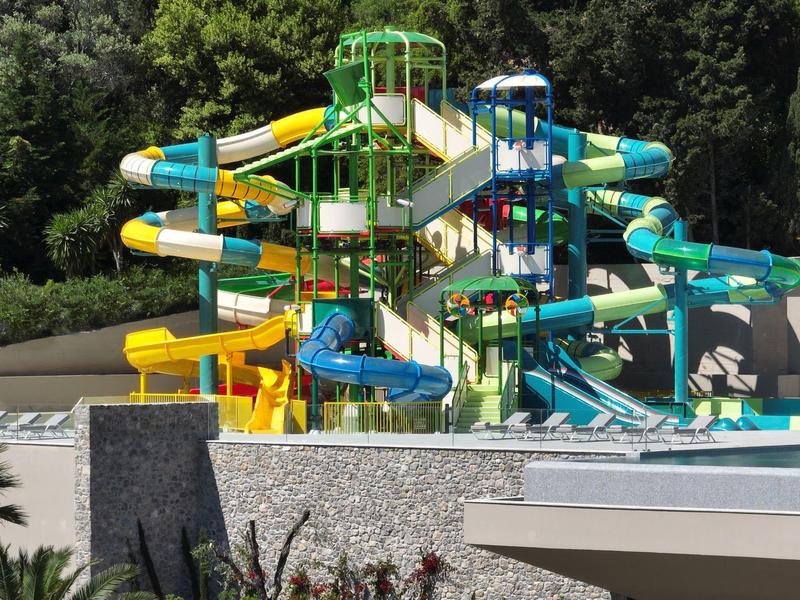 Mehrstöckige bunte Wasserrutschen in einem Freizeitpark, umgeben von Bäumen und Gebäuden.