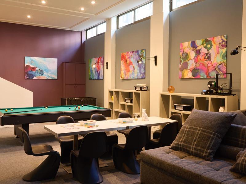 Modern eingerichteter Spiel- und Aufenthaltsraum mit Billardtischen, Kunstwerken und gemütlichem Sofa.