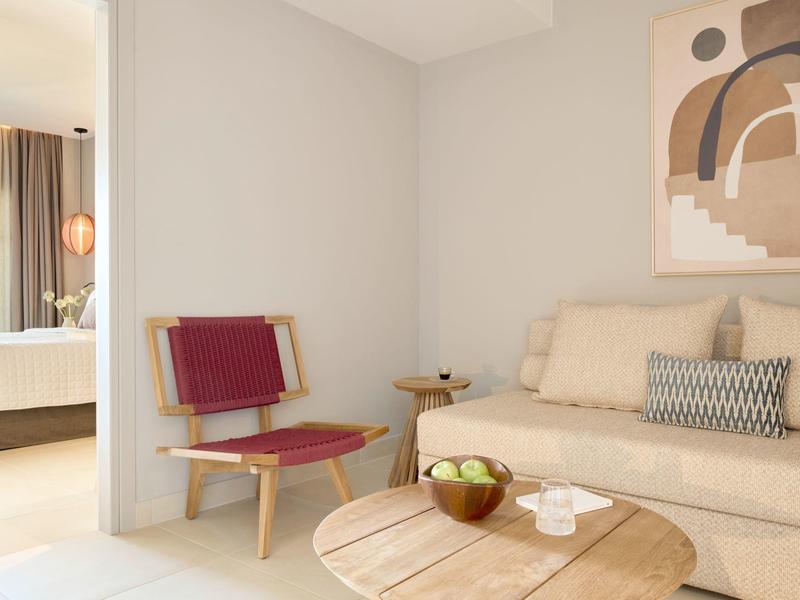 Moderner Wohnraum mit hellen Wänden, beige Couch, rundem Holztisch und rotem Stuhl.