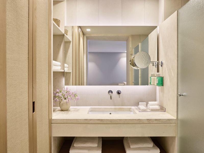 Helles, modernes Badezimmer mit großem Spiegel, Waschbecken, Holzregalen und weicher Beleuchtung.