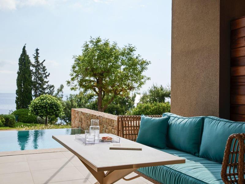 Terrasse mit blauem Sofa, Holztisch, Pool und Blick auf Bäume und Meer im Hintergrund.