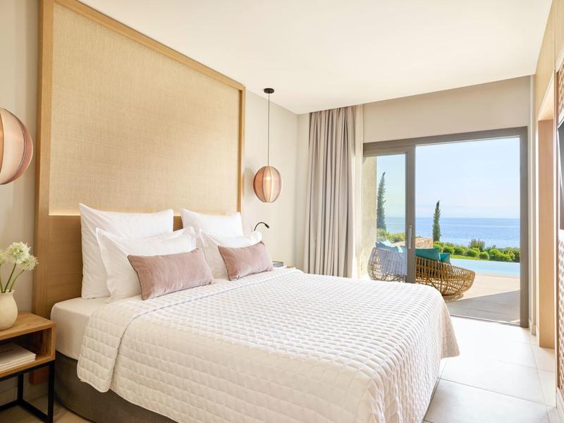 Helles Schlafzimmer mit großem Bett, Holzrahmen, runden Lampen und Meerblick durch große Fenster.