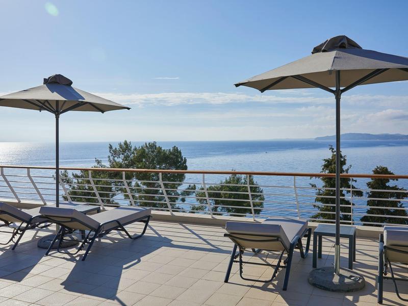 Terrasse mit Liegestühlen, Sonnenschirmen und Blick auf das blaue Meer und den klaren Himmel.