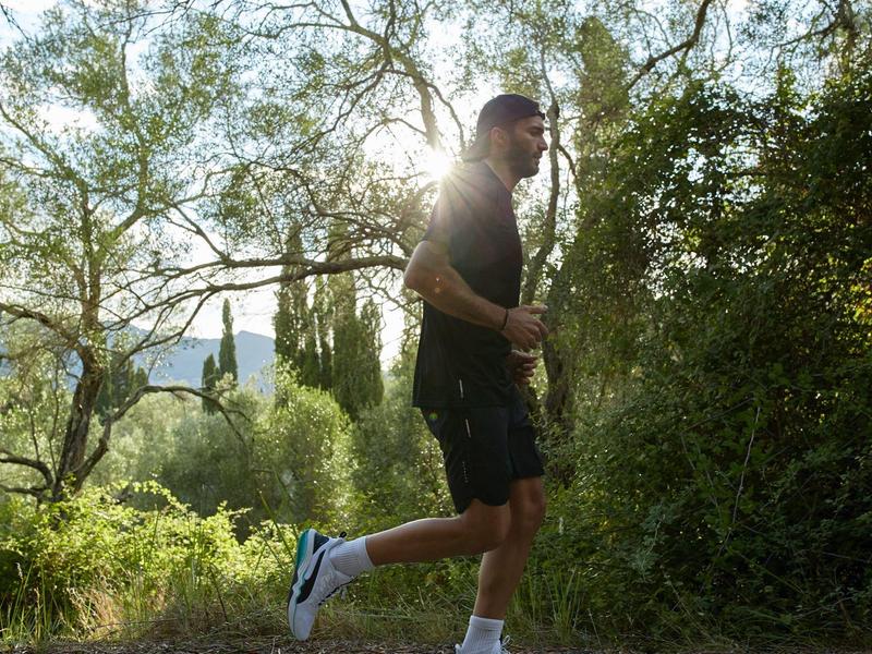 Mann joggt auf sonnigem Waldweg, umgeben von grünen Bäumen und Pflanzen.