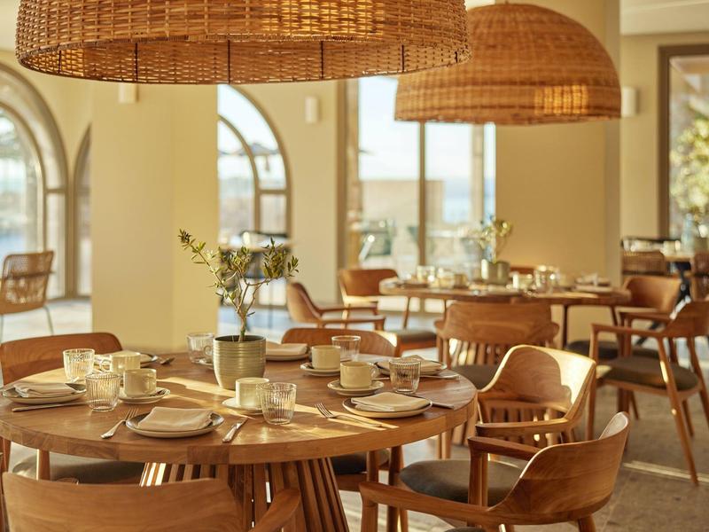 Elegantes Restaurant mit runden Holztischen, weichen Stühlen und großen geflochtenen Lampen.