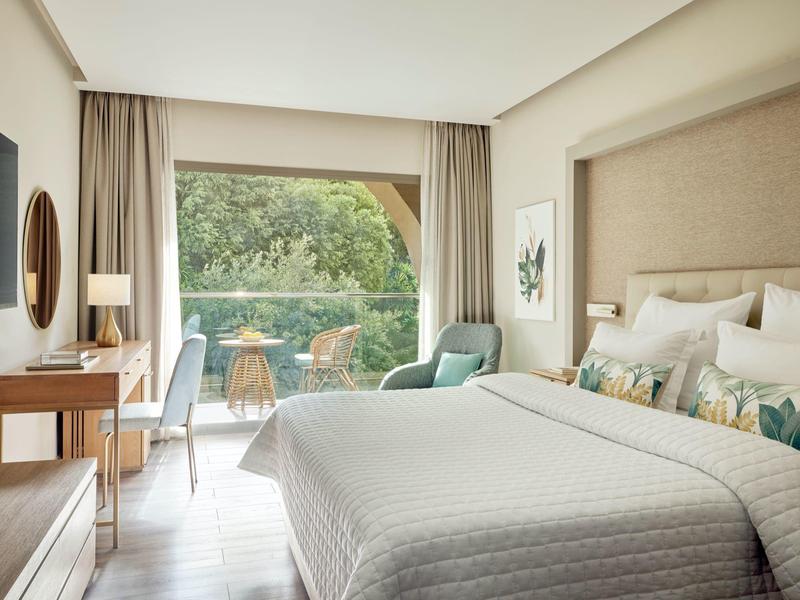 Modernes Schlafzimmer mit großem Bett, grünem Sessel, Schreibtisch und großem Fenster zur Terrasse.