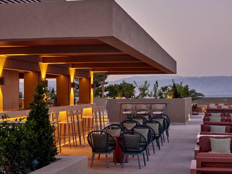 Moderne Terrasse mit Bar, Stühlen und Tischen, Blick aufs Meer bei Abenddämmerung.