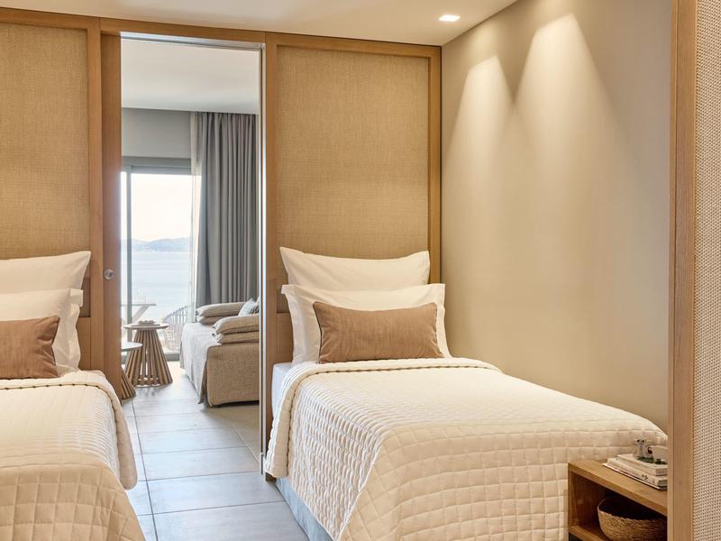 Modernes Schlafzimmer mit zwei Einzelbetten, beiger Wand, Spiegel und hellen Vorhängen.