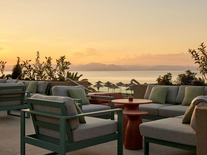 Terrassenmöbel mit Polsterung vor Meerblick bei Sonnenuntergang mit orangefarbenem Himmel.