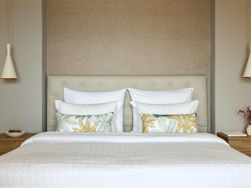 Schlichtes Schlafzimmer mit weißem Bett, zwei Blumenmustern auf Kissen und minimalistischem Holztisch.