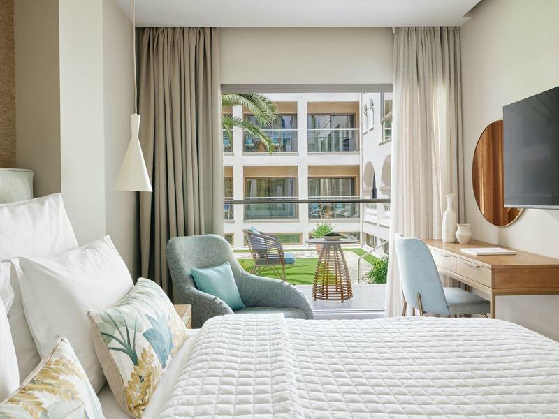 Modern eingerichtetes Schlafzimmer mit Bett, blauen Sesseln, Schreibtisch und Balkonblick.