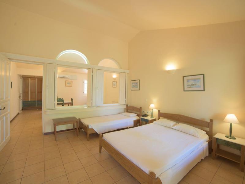 Helles Schlafzimmer mit zwei Betten, weißen Wänden, Kachelfußboden und einfachen Möbeln.