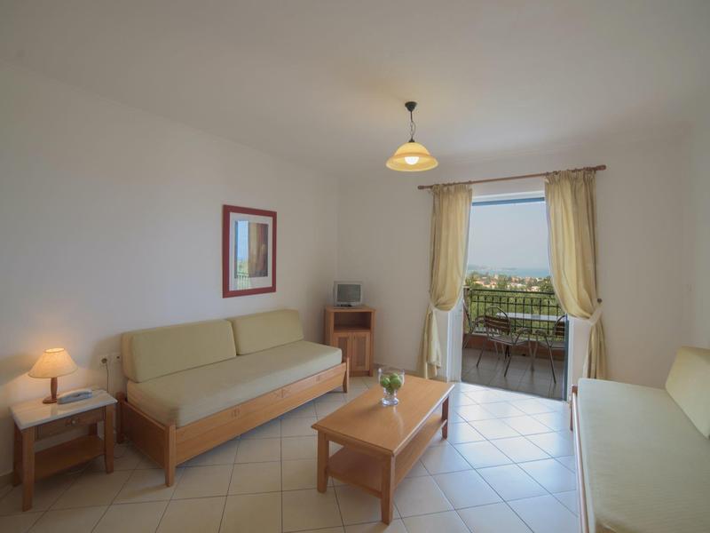 Heller Wohnraum mit zwei Sofas, Holztisch, Nachttisch, Lampe und offenem Balkon mit Blick ins Grüne.