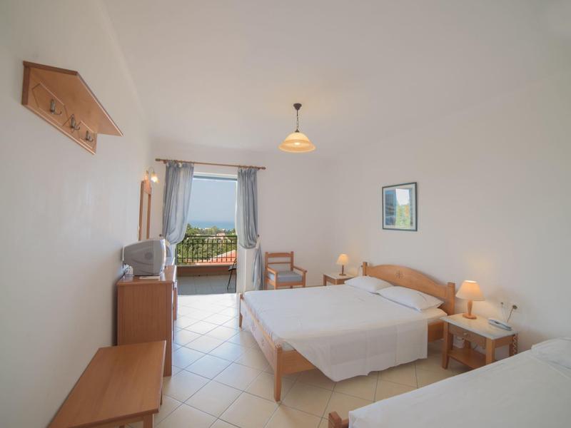 Helles Schlafzimmer mit zwei Doppelbetten, Holzmöbeln, Fliesenboden und Blick auf einen Balkon.