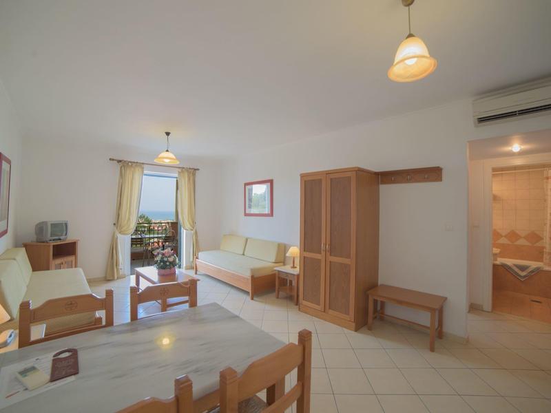 Helles Wohnzimmer mit Holzmöbeln, Sofa, Esstisch und Zugang zu Balkon und Badezimmer.