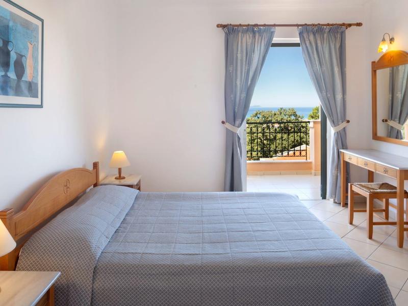 Helles Schlafzimmer mit großem Bett, grauer Decke, Nachttischlampen und Balkon mit Meerblick.