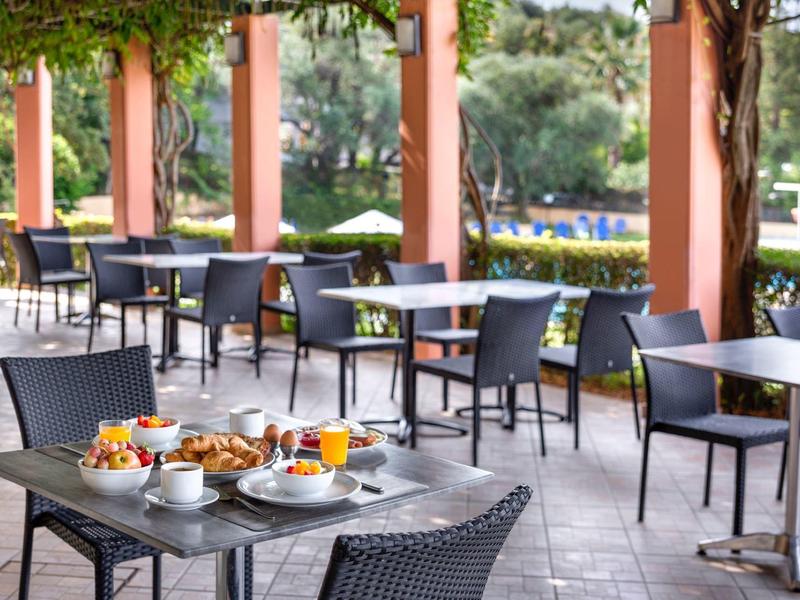 Freiluftrestaurant mit schwarzen Stühlen, Tischen und gedeckten Plätzen im sonnigen Ambiente.