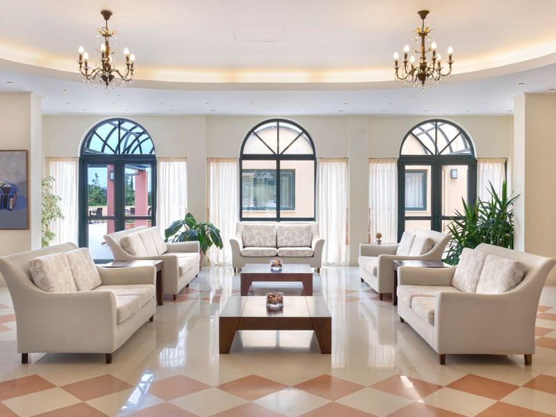 Helles Wohnzimmer mit weißen Sofas, großen Fenstern, Holztisch und cremefarbenem Bodenmuster.