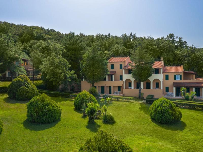 Großes Haus mit roten Dächern umgeben von grünem Rasen und vielen kleinen, runden Sträuchern.