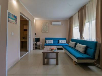 Heller Wohnraum mit blauen Sofas, kleinem Tisch und großen Fenstern mit hellen Vorhängen.