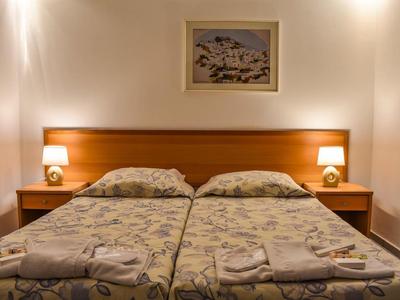 Zwei Einzelbetten mit gemusterten Bettlaken, zwei Nachttische mit Lampen, helles Bild darüber.