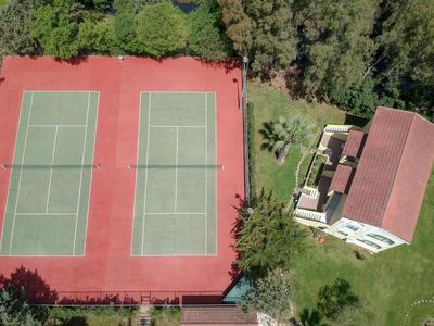 Vista aérea de dos canchas de tenis junto a un edificio en una zona verde.
