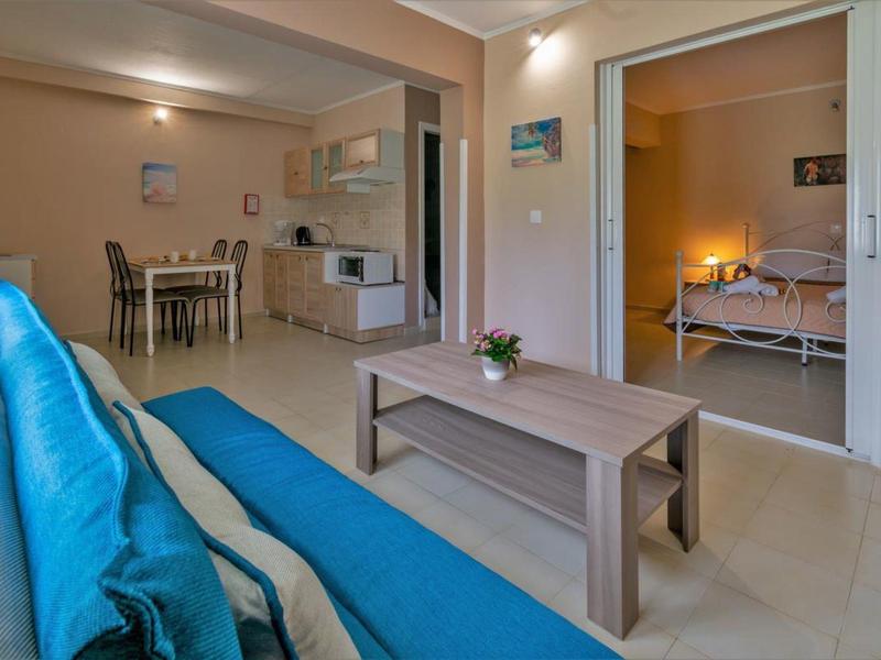 Moderner Wohnraum mit blauem Sofa, Holztisch und angrenzendem Essbereich sowie Schlafzimmer.