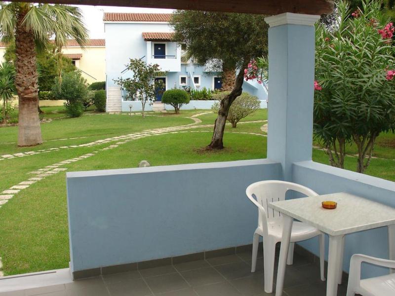 Terrasse mit weißem Tisch und Stühlen, Blick auf gepflegten Garten mit Palmen und Weg.