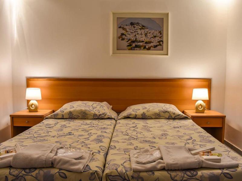 Zwei Einzelbetten mit gemusterten Bettlaken, zwei Nachttische mit Lampen, helles Bild darüber.