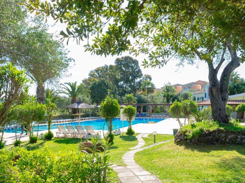 Grüner Garten mit Bäumen und einem blauen Pool, umgeben von Sonnenschirmen und Liegestühlen.