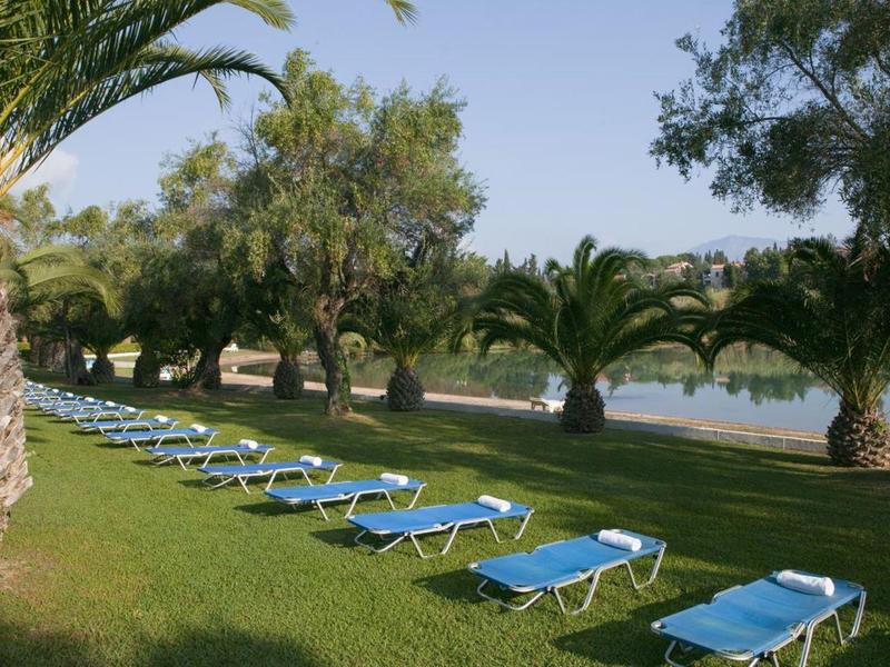 Eine Reihe blauer Liegestühle auf grünem Rasen neben Wasser und Palmen.