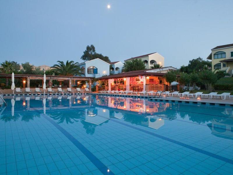 Großer Pool bei Dämmerung vor einem beleuchteten Restaurant mit Liegestühlen und Bäumen.