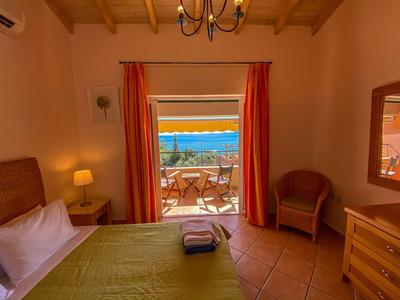 Gemütliches Hotelzimmer mit Doppelbett und Balkon mit Meerblick bei Sonnenuntergang.