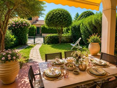 A set dining table under a covered area overlooking a well-kept garden and lounge chair.
