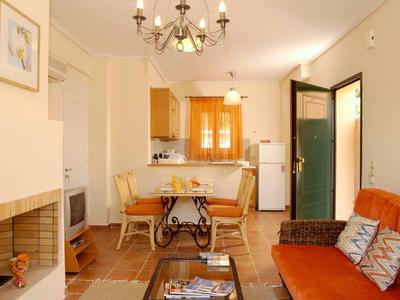 Gemütliches Wohnzimmer mit orangenem Sofa, Holztisch, Kamin und offener Küche mit Esstisch.