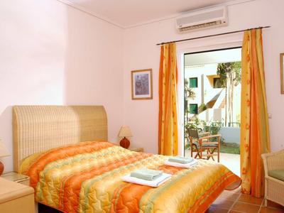 Schlafzimmer mit Einzelbett in orangefarbenen Tönen, Fenster mit gelben Vorhängen und Zugang zu Terrasse.