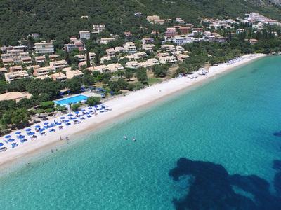 Beach with turquoise water, sun umbrellas, and hotels nestled in green surroundings.